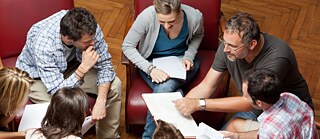 Eine Gruppe Personen sitzt zusammen und bespricht etwas, alle halten Notizen in den Händen.