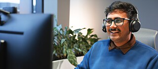 Ein Mann mit Kopfhörern lächelt, während er auf den Computerbildschirm schaut.