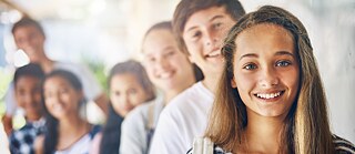 A teenage girl smiling into the camera standing in front of a group of peers.