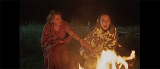 Zwei Frauen, in Decken eingehüllt sitzen an einem Feuer