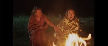 Zwei Frauen, in Decken eingehüllt sitzen an einem Feuer