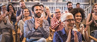 Menschen nehmen an einem Seminar teil. Sie sitzen im Konferenzraum und klatschen lachend in die Hände.
