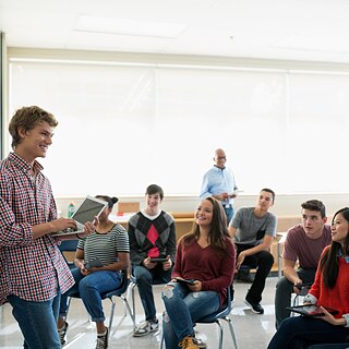 Schüler hält vor Kommilitonen eine Präsentation mit dem Laptop.