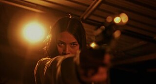 A woman points the pistol directly at the camera. 