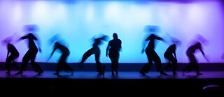 Eine Tanzperformance. Tanzende Schattenrisse in lila-türkisem Licht.