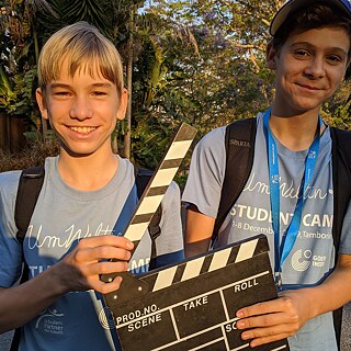 Zwei Jugendlich strahlen in die Kamera und halten eine Filmklappe in den Händen