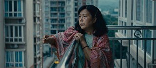 Rauchende ältere Frau auf einem Balkon zwischen Hochhäusern