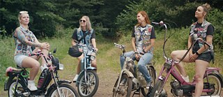 Vier Frauen mit Fußballkutten auf ihren Mopeds