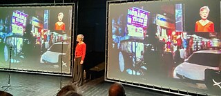 Performer Bettina Marugg in Bonn in front of a video projection during the performance in November. She describes the scene with texts from interviews. 