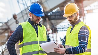   Ingenieure, die auf einer Baustelle Projektdokumente betrachten und den Bauprozess besprechen. 
