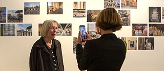 Im Vordergrund: die Künstlerin Christina Kubisch bei der Eröffnung der Ausstellung "Electrical Jubilee" am 23.05.2025 im Goethe-Institut Rom; im Hintergrund ausgestellte Fotos auf weißer Wand