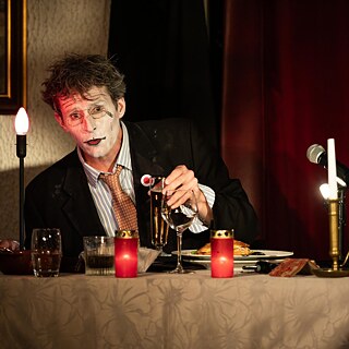 Ein Mann sitzt mit Speisen und Getränken an einem von Kerzen erleuchteten Tisch