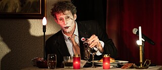 Ein Mann sitzt mit Speisen und Getränken an einem von Kerzen erleuchteten Tisch