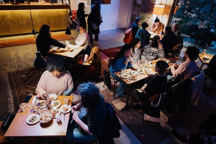 Al Meyhane i tavoli sono imbanditi con stuzzichini e antipasti da condividere tra persone che mangiano e conversano.