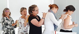 Lehrkräfte stehen hintereinander und schreiben jeweils auf den Rücken der vor Ihnen stehenden Person