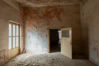 A room in an abandoned building where the floor is filled by rubble breaking off the ceiling’s plaster because of neglection and weather impact