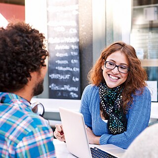 Un grupo está sentado afuera, frente a un café, en una mesa, conversando animadamente.