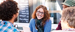 Un grupo está sentado afuera, frente a un café, en una mesa, conversando animadamente.