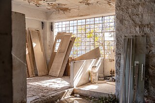 Eine Ecke eines verlassenen Gebäudes mit demontierten Türen und Sonnenlicht, das durch ein fensterloses Fenster fällt.