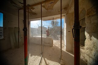 Ein Mann sandstrahlt eine verlassene Decke in einem sonnigen Raum.