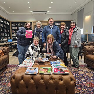 Lehrkräfte stehen in einer Bibliothek und zeigen Lehrzeitschriften und Bücher