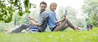 Ein junger Mann und eine junge Frau lernen auf einer Wiese