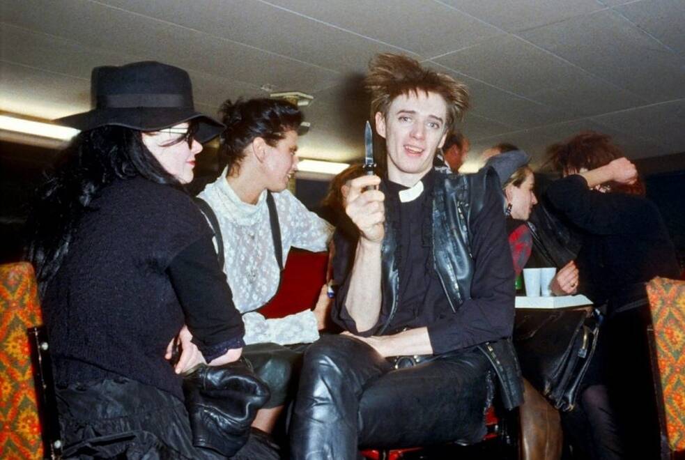 B-Movie (Deutschland, 2015, 92 Min.) Regie: Jörg A. Hoppe, Klaus Maeck, Heiko Lange, Miriam Dehne. Das Standbild zeigt Blixa Bargeld inmitten einer Gruppe vorwiegend dunkel gekleideter junger Leute wie er ein Messer zückt.