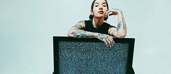  Person sitting behind a television with static noise; arms loosely draped over the screen.