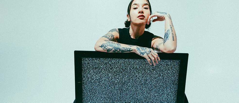 Person sitting behind a television with static noise; arms loosely draped over the screen.