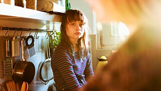 Noor naine istub köögis. Taustal ripuvad köögitarbed