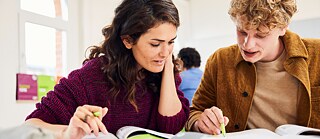 Zwei Personen sitzen an einem Tisch und lernen gemeinsam aus aufgeschlagenen Büchern.