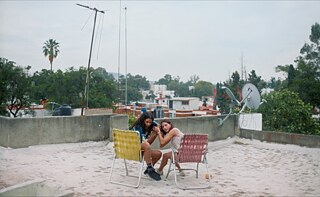 Dos adolescentes sentadas en la azotea escuchando un dispositivo, en "Chicas Tristes" de Fernanda Tovar. 