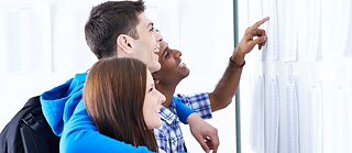 Student*innen lesen Informationen an Anschlagbrett.