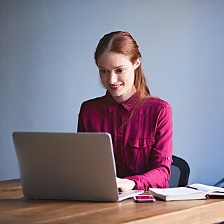 Молода жінка сидить в офісі за столом із ноутбуком і посміхається.