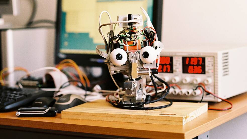 Standbild aus „Plug & Pray“ (Jens Schanze, 2010), einer Dokumentation über die Versprechen, Herausforderungen und ethischen Konflikte rund um künstliche Intelligenz und Robotik. Der Film thematisiert die Vision einer Symbiose von Mensch und Maschine, die es ermöglichen soll, die biologischen Grenzen der Evolution hinter sich zu lassen, bis hin zur Idee der technischen Unsterblichkeit. Im Zentrum stehen der ehemalige MIT‑Professor Joseph Weizenbaum und der Futurist Raymond Kurzweil.