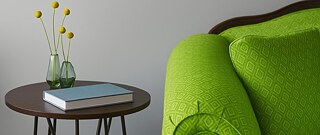 Grüne Couch neben einem kleinen Tisch mit Vase und Blumen.