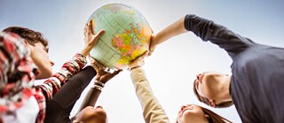 Several young people hold up a globe together. Shot from below against the sky.