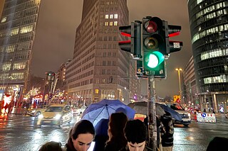 Eine regennasse Straßenkreuzung bei Nacht, einige junge Leute im Vordergrund