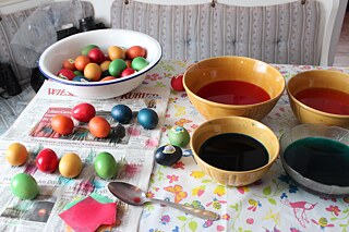 Ein Tisch mit verschiedenen Farben in verschiedenen Schüsseln. Daneben frisch gefärbte Eier, die auf Zeitungspapier trocknen.