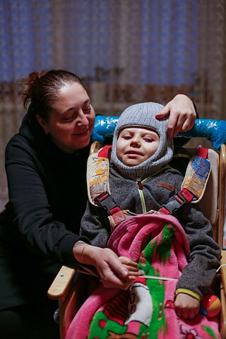 Lena lebt mit ihrem Sohn Vladymyr und ihrer Tochter Svitlana in Kyjiw in einer Wohnung im 13. Stock. Während der Bombenangriffe verstecken sie sich im Flur, da die Aufzüge bei Stromausfall nicht funktionieren.