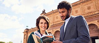  Zwei Teilnehmende beim gemeinsamen Kulturprogramm. Sie stehen vor der Kunsthalle und sehen sich gemeinsam ein Buch an.