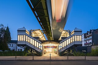 Ein Zug fährt im Abendlicht in die Schwebebahnstation Völklinger Straße ein.