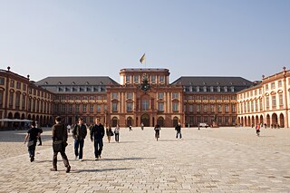 Blick auf den Mittelbau des Schlosses, auf dem Hof im Vordergrund flanieren junge Menschen.