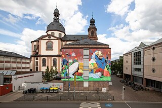 Ein Grafitti zeigt einen imposanten Löwen in einer ruhenden Position, umgeben von abstrakten Pflanzenfragmenten.