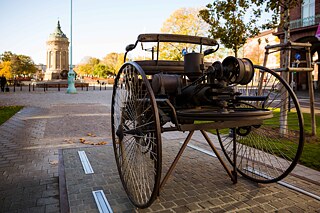Denkmal für Carl Friedrich Benz in der Augusta-Anlage in Mannheim, gegenüber dem Friedrichsplatz, im Vordergrund Nachbau des Benz-Patent-Motorwagen.