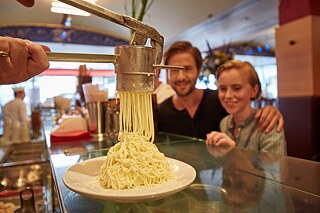 Eis wird durch eine gekühlte Spätzlepresse gedrückt, ein junger Mann und ein Kind sehen begeistert zu.