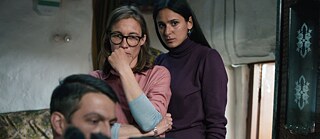 Szene aus dem Film „Im toten Winkel“: In einem Raum stehen zwei Frauen, und im Vordergrund sieht man den Kopf eines Mannes, der am Computer sitzt.