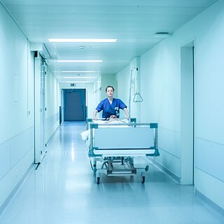 Filmstill fra Aftenvagt. En sygeplejerske skubber en seng ned ad en lang gang.