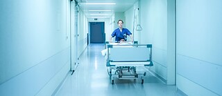 Filmstill fra Aftenvagt. En sygeplejerske skubber en seng ned ad en lang gang.