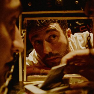 Filmstill fra "Rave On": En mand kigger ind gennem et lille dørvindue. 